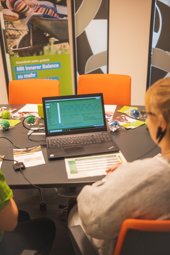 Frau mit Messgerät am Ohr vor einem Laptop